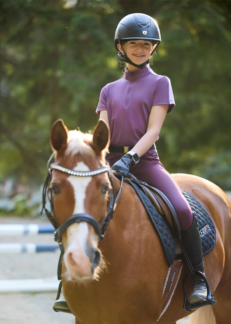 Front view of a young female model wearing the purple Kerrits Kids Coolcore Full Seat Tech Tights while riding a chestnut horse