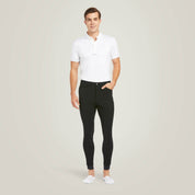 Full body front view of a male model wearing the Black Ariat Men's Tri Factor Knee Patch Breeches with a white shirt on a plain background