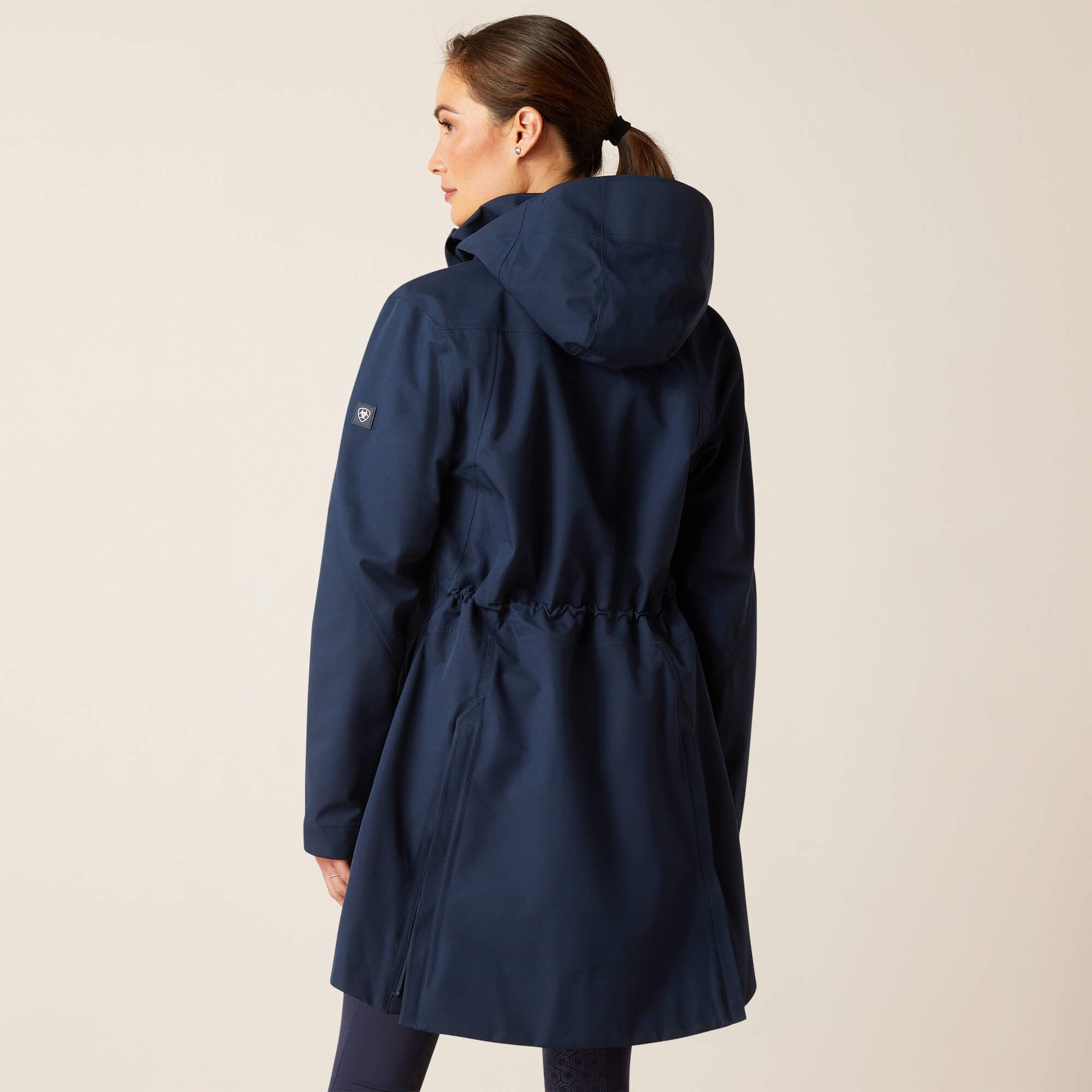 Back view of a female model wearing the Navy Ariat Coastal Long H2O Parka on a plain background