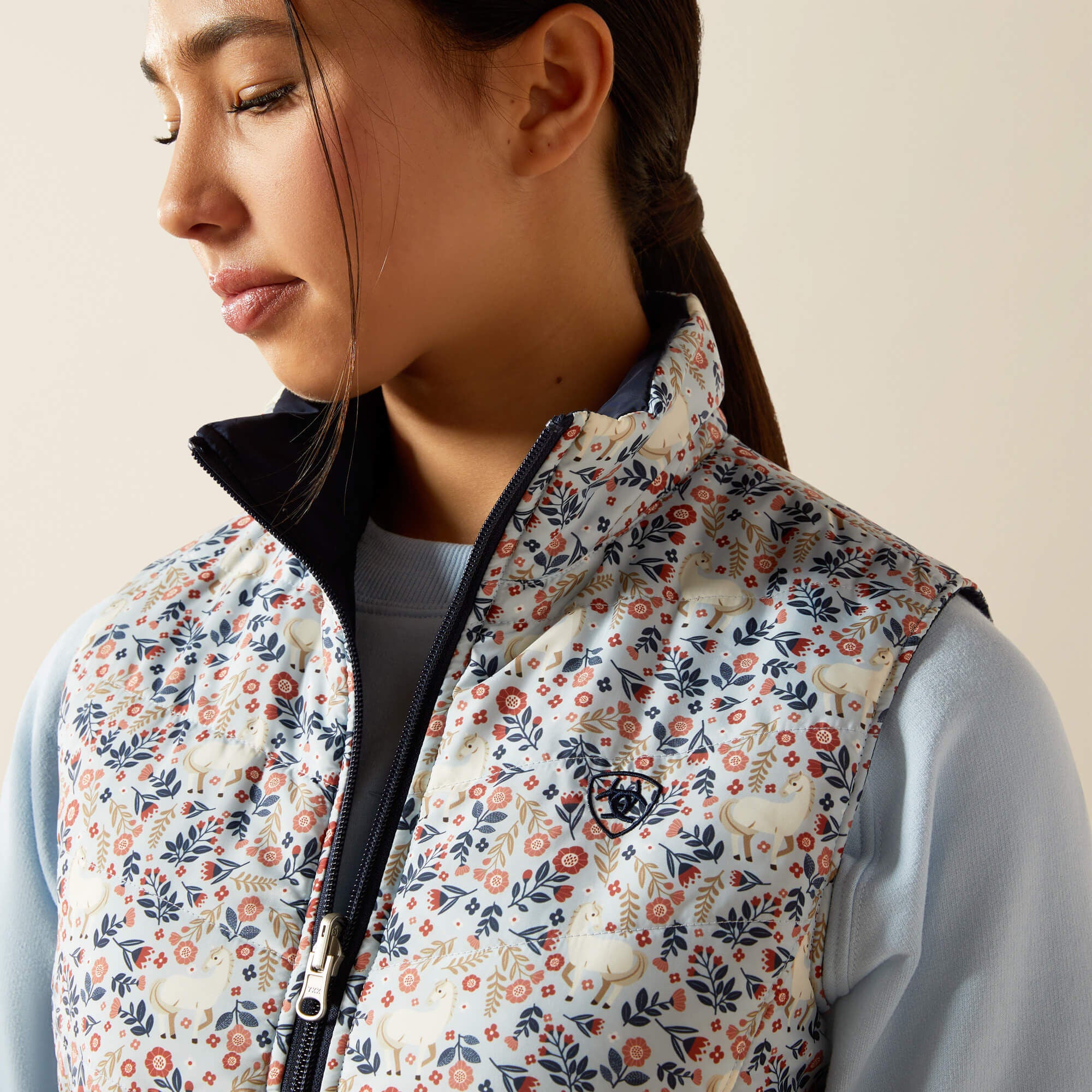Close-up front view of a young female model wearing the Posey Pony Print Ariat Youth Bella Reversible Insulated Vest on a plain background