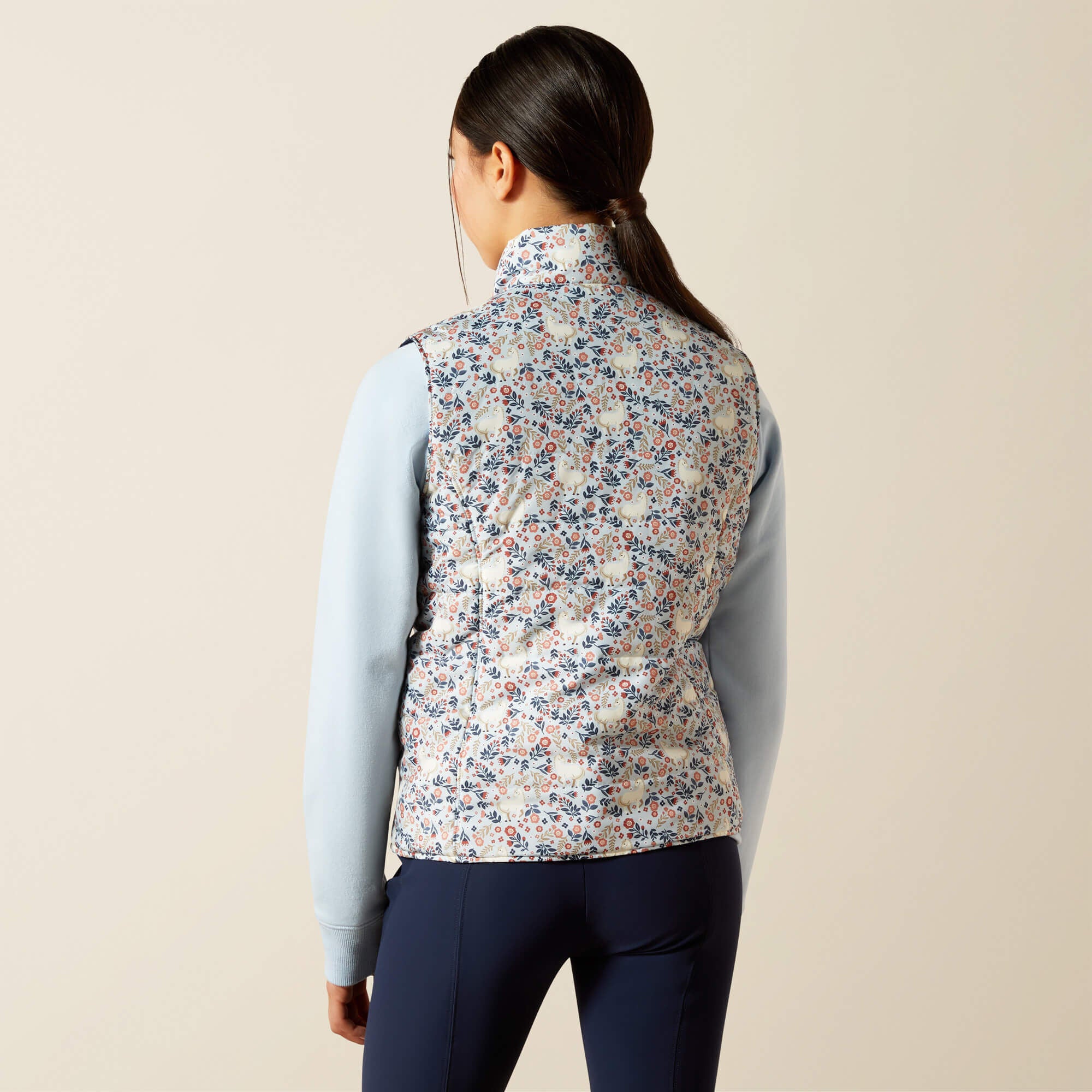Back view of a young female model wearing the Posey Pony Print Ariat Youth Bella Reversible Insulated Vest on a plain background