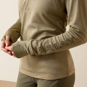 Angled front closeup view of a model wearing the Winter Twig Ariat Team EQ 1/2 Zip Pullover on a plain background showing the lettering on the sleeve and the thumbhole cuffs
