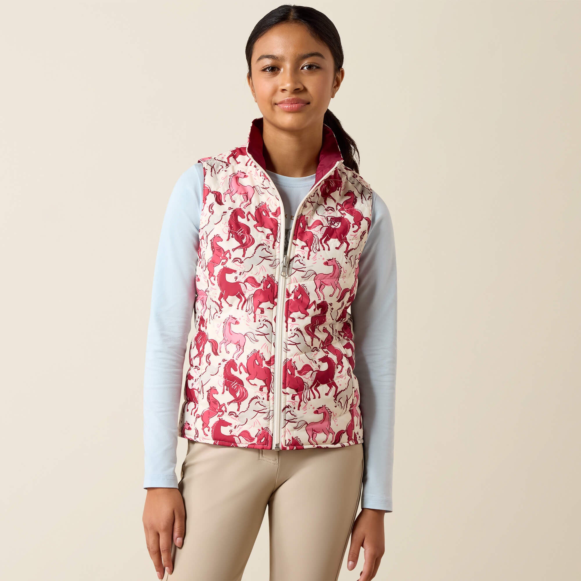 Front view of a young female model wearing the Vanilla Ice Horsin' Around Ariat Youth Bella Reversible Insulated Vest on a plain background