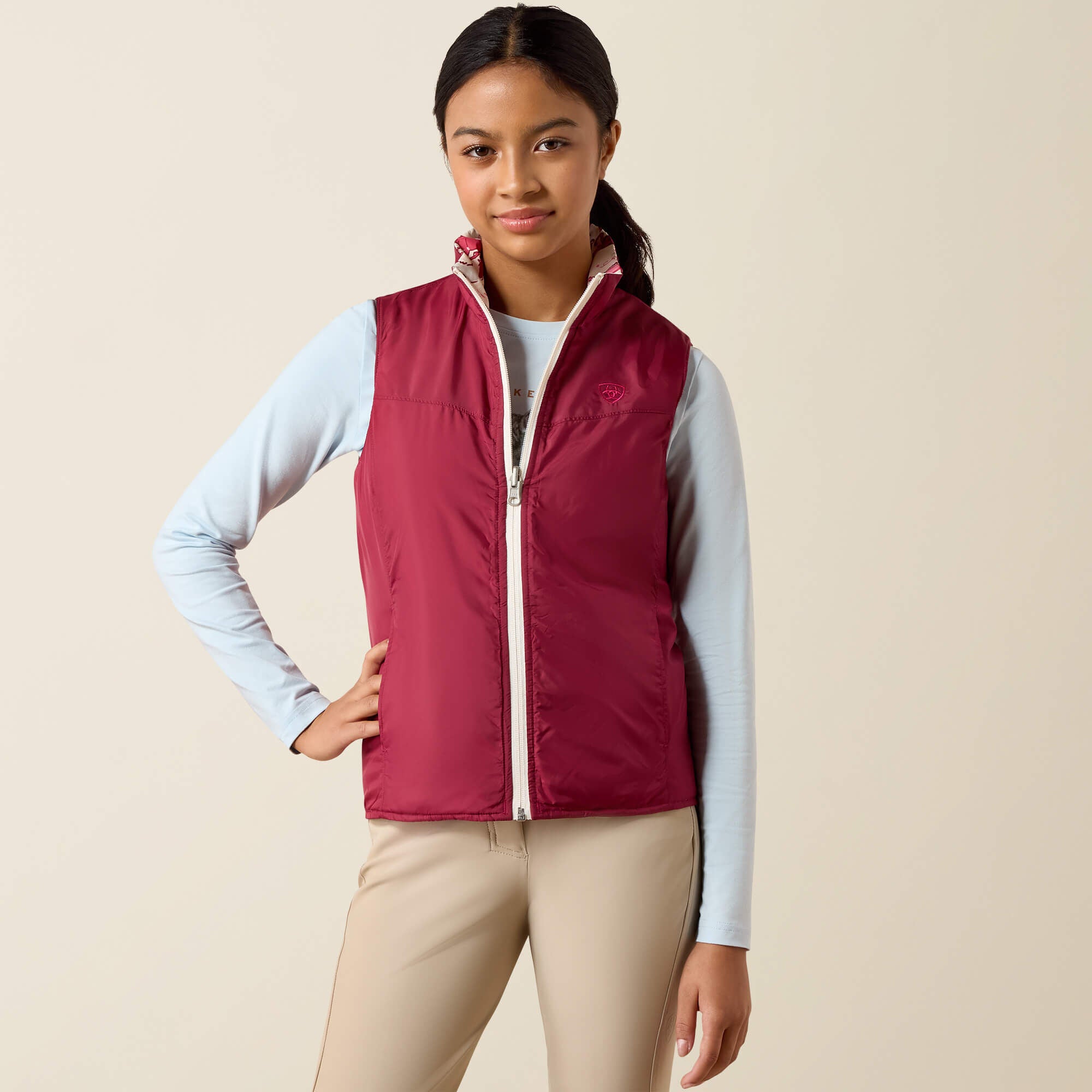 Front view of a young female model wearing the Vanilla Ice Horsin' Around Ariat Youth Bella Reversible Insulated Vest on a plain background