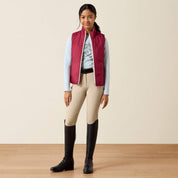 Full body front view of a young female model wearing the Vanilla Ice Horsin' Around Ariat Youth Bella Reversible Insulated Vest with tan breeches on a plain background