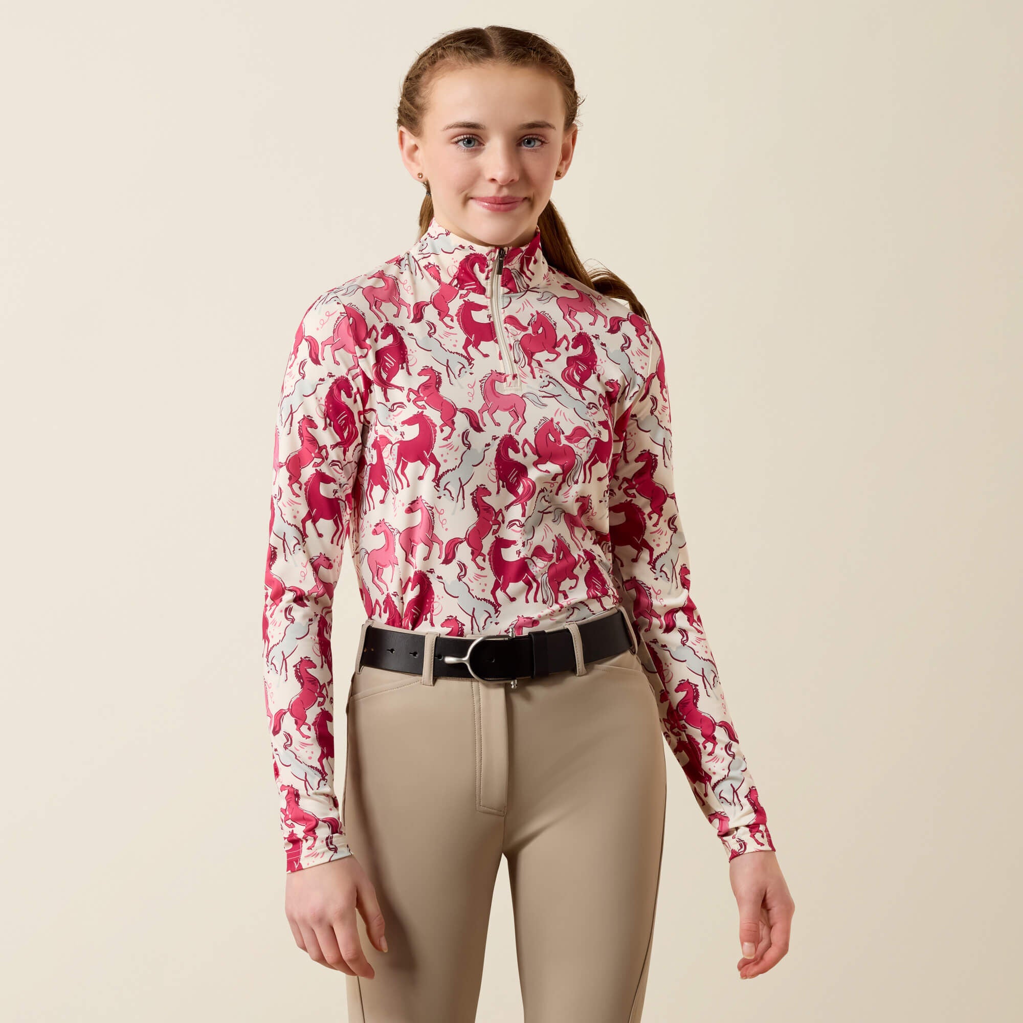 Front view of a young female model wearing the Vanilla Horsin' Around Print Ariat Youth Lunaveil 1/4 Zip Long Sleeve Baselayer on a plain background