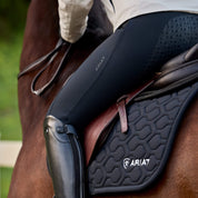 Angled back view of a female model wearing the Black Ariat Troika H2O Full Seat Breeches while riding a horse outside