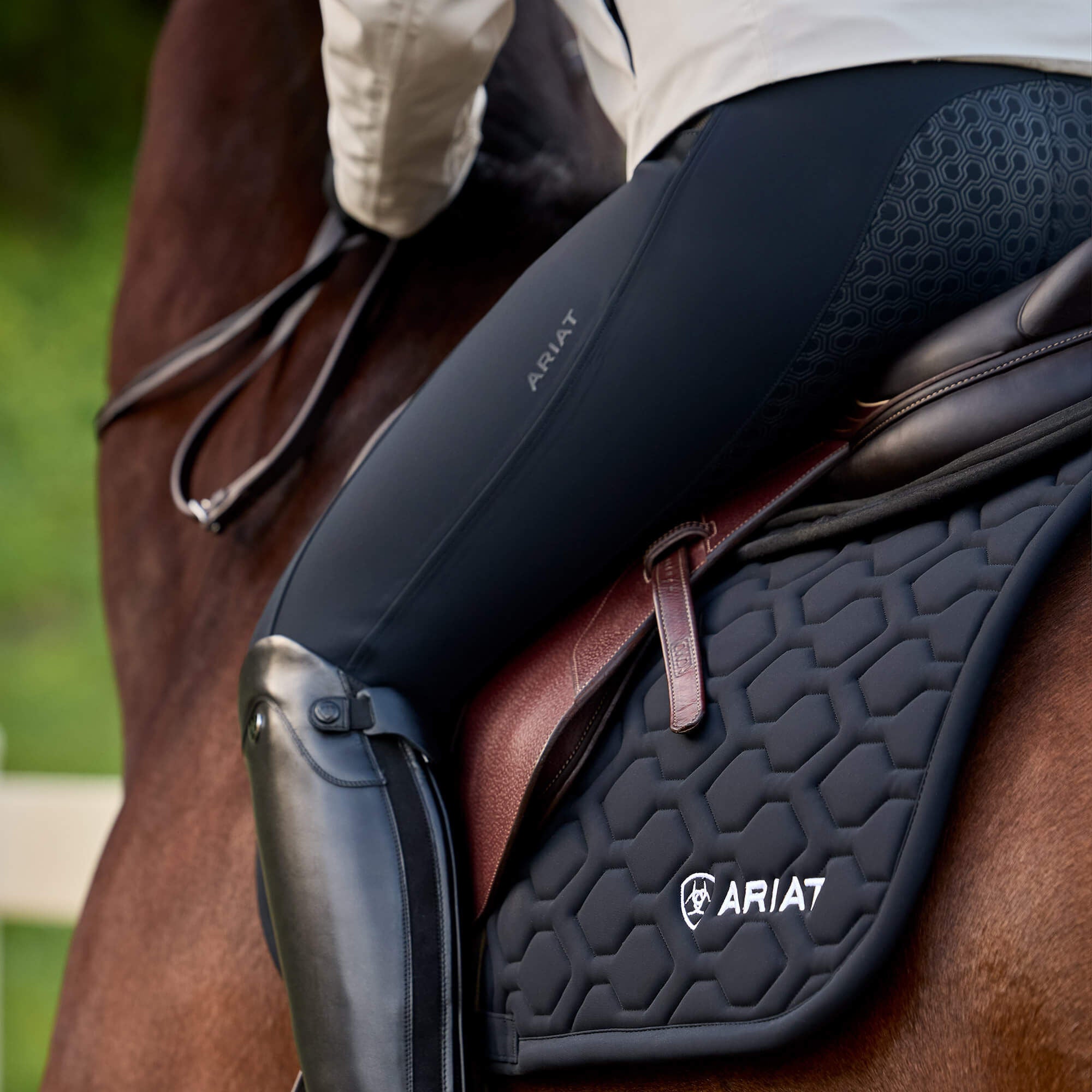 Angled back view of a female model wearing the Black Ariat Troika H2O Full Seat Breeches while riding a horse outside