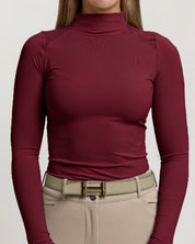 View of a female model wearing the Rich Burgundy TKEQ Chloe High Collar Technical Top on a plain background