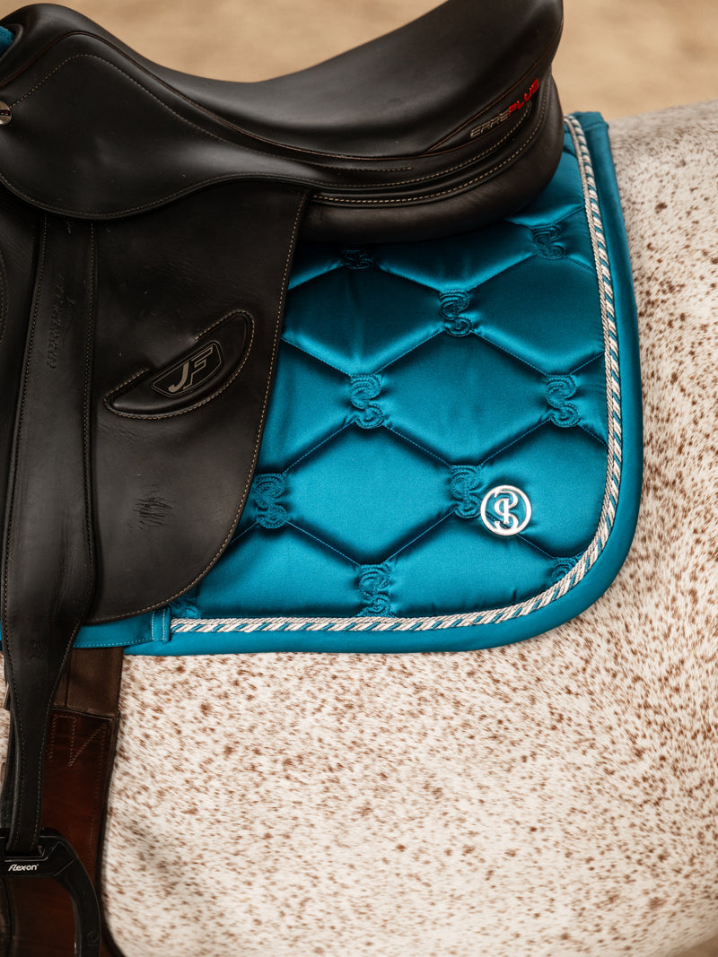 Close-up view of the logo on the Evening Teal PS of Sweden Signature Jump Pad as worn by a gray horse