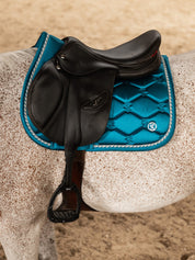 Side view of a gray horse wearing the Evening Teal PS of Sweden Signature Jump Pad while standing in an indoor arena