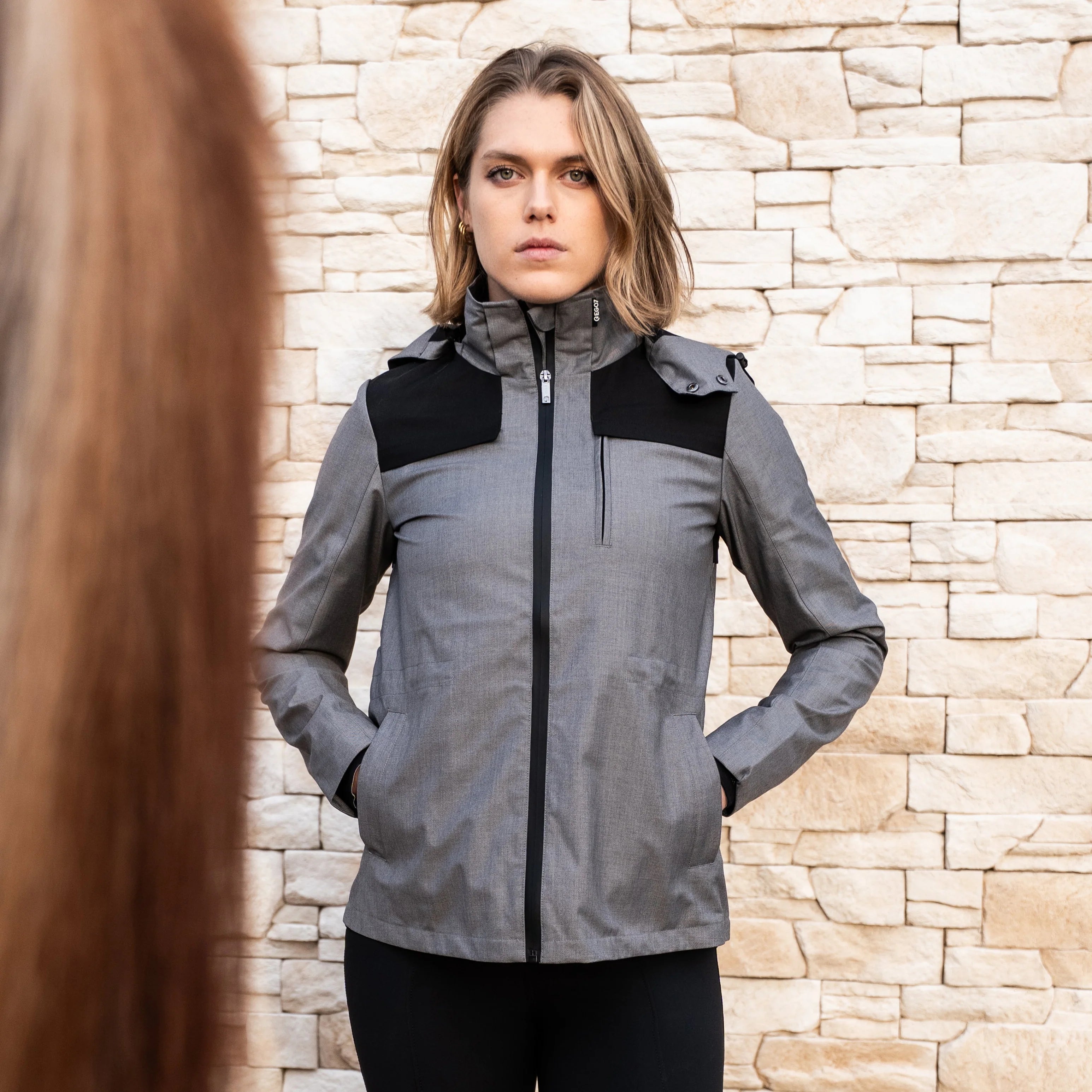 Grey Full zip hooded rain jacket with black panels and accents shown on model in front of brick barn