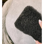 Close-up view of the Epona Tiger's Tongue Horse Groomer with a white horse's hindquarters in the background