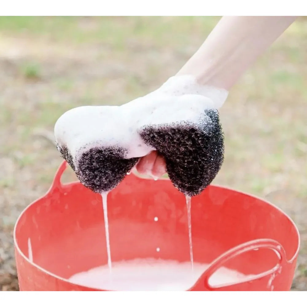 View of someone squeezing a soapy Epona Tiger's Tongue Horse Groomer into a red bucket of suds