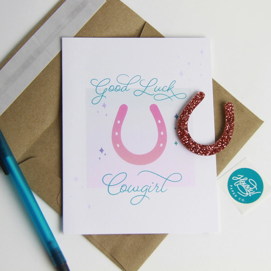 Front view of the Good Luck, Cowgirl Hunt Seat Paper Co. Greeting Card with its envelope and charm