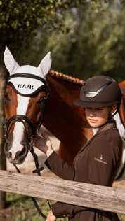 View of a female model standing next to a horse, whole the female model is wearing the Brown KASK Star Lady Chrome Helmet