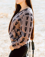 Side view of a female model wearing the Saddle/Black Deinhardt Designs Varsity Sweater while standing outside