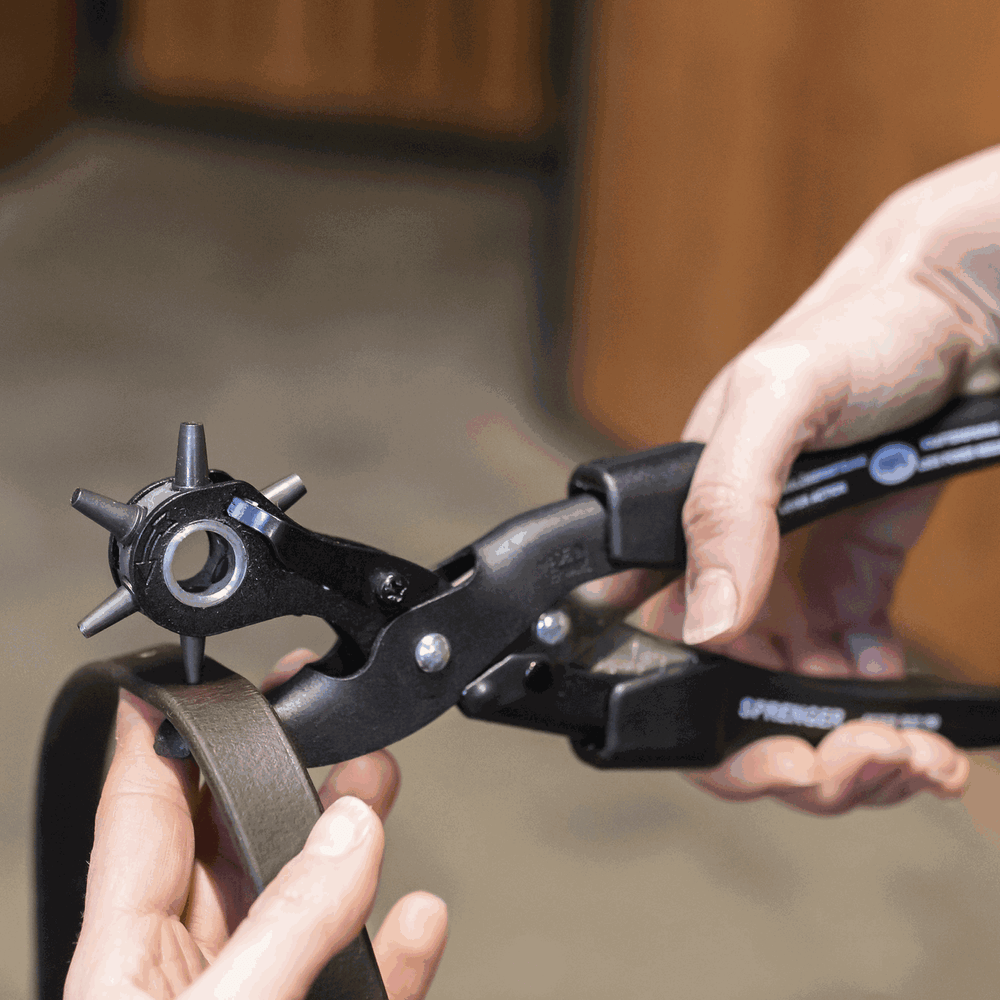 Close-up view of someone using the Herm Sprenger Extra-Power Revolving Leather Punch to punch a hole in a leather strap