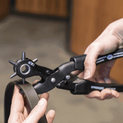 Close-up view of someone using the Herm Sprenger Extra-Power Revolving Leather Punch to punch a hole in a leather strap