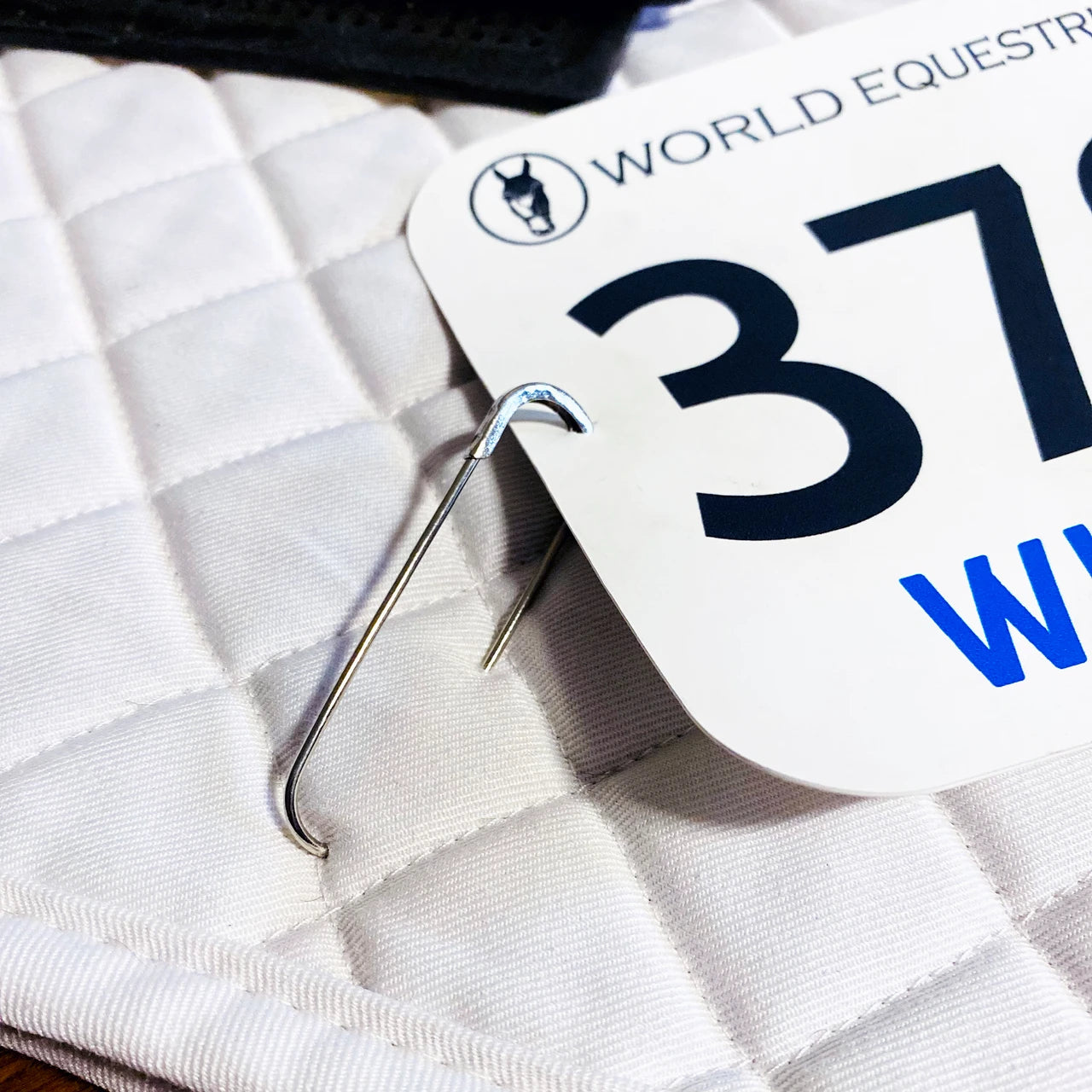 View of a Pro4mance Show Number Pin attaching a number to a white saddle pad