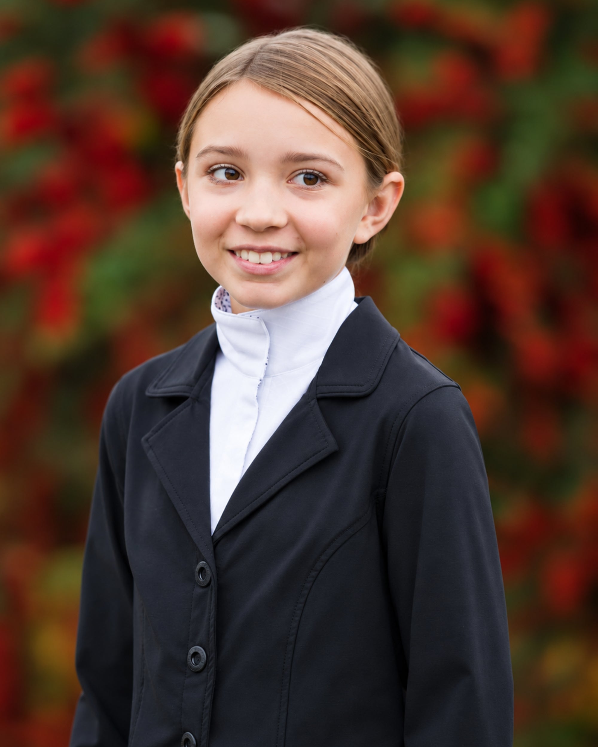 Front view of a young female model wearing the Black Kerrits Kids Stretch Competitor Show Coat on a colorful background