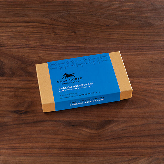 View of the 8 piece gift box of the Harbor Sweets Dark Chocolate English Assortment on a wood background