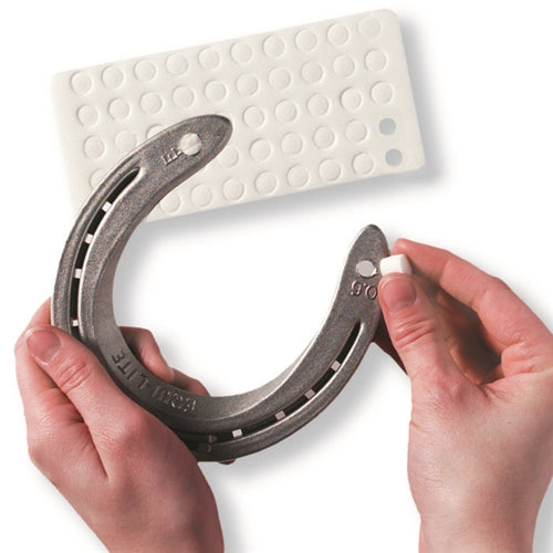 View of someone inserting a Nunn Finer Thread Saver Stud Hole Plug into a horseshoe on a white background