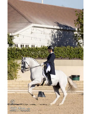 View of a model riding a white horse that is wearing the NSC Natural Sheepskin Moon Dressage Girth in an outdoor arena