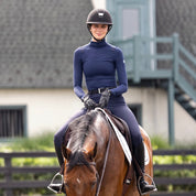 Front view of a female model wearing the Ink TKEQ Chloe High Collar Technical Top while riding a bay horse