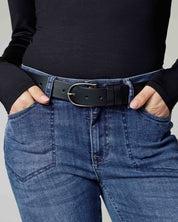 Close-up front view of a female model wearing the black/silver Amsterdam Heritage Dieke Classic Leather Belt with blue jeans on a plain background