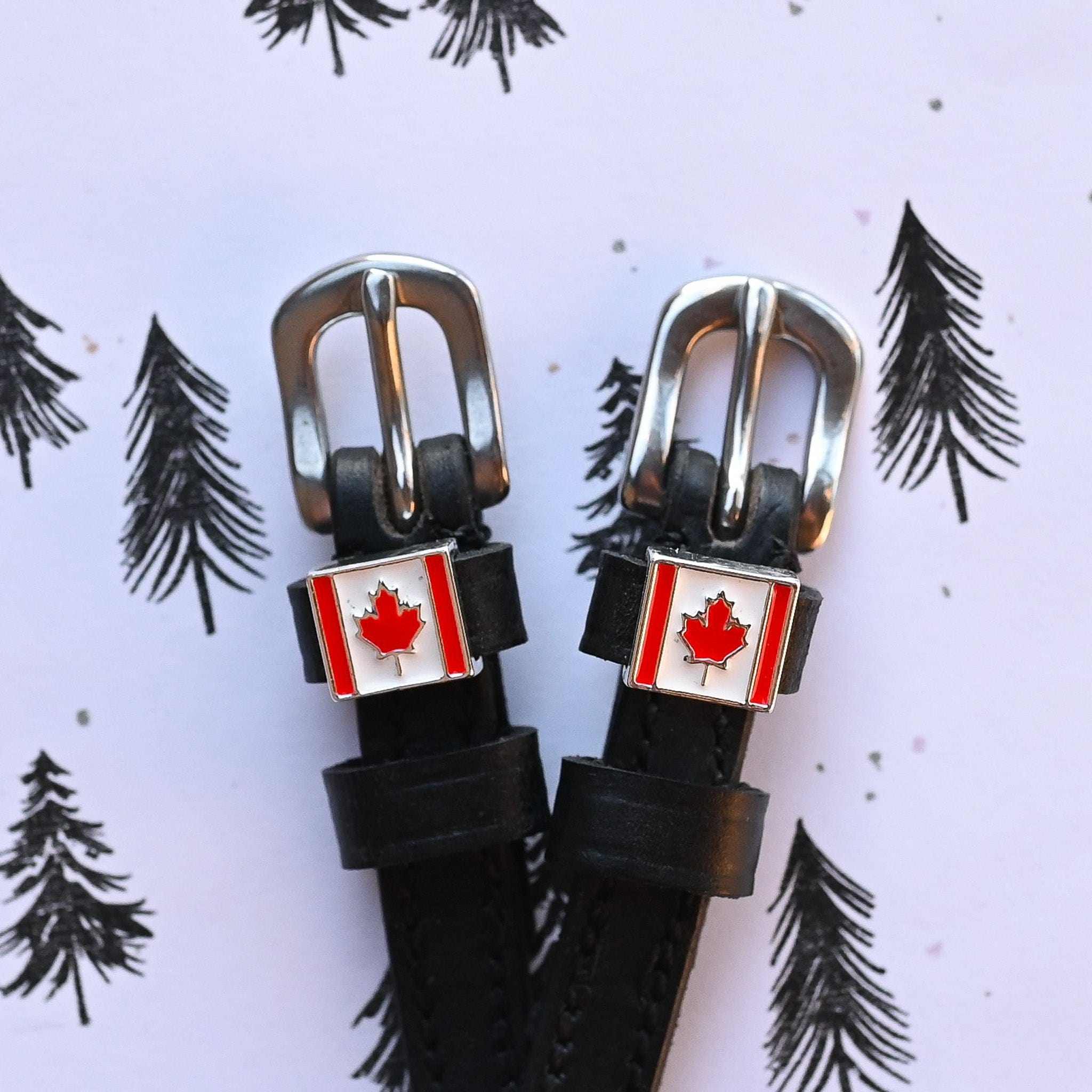 View of the Canadian flag Mane Jane Spur Straps  on a purple background with pine tree sketches