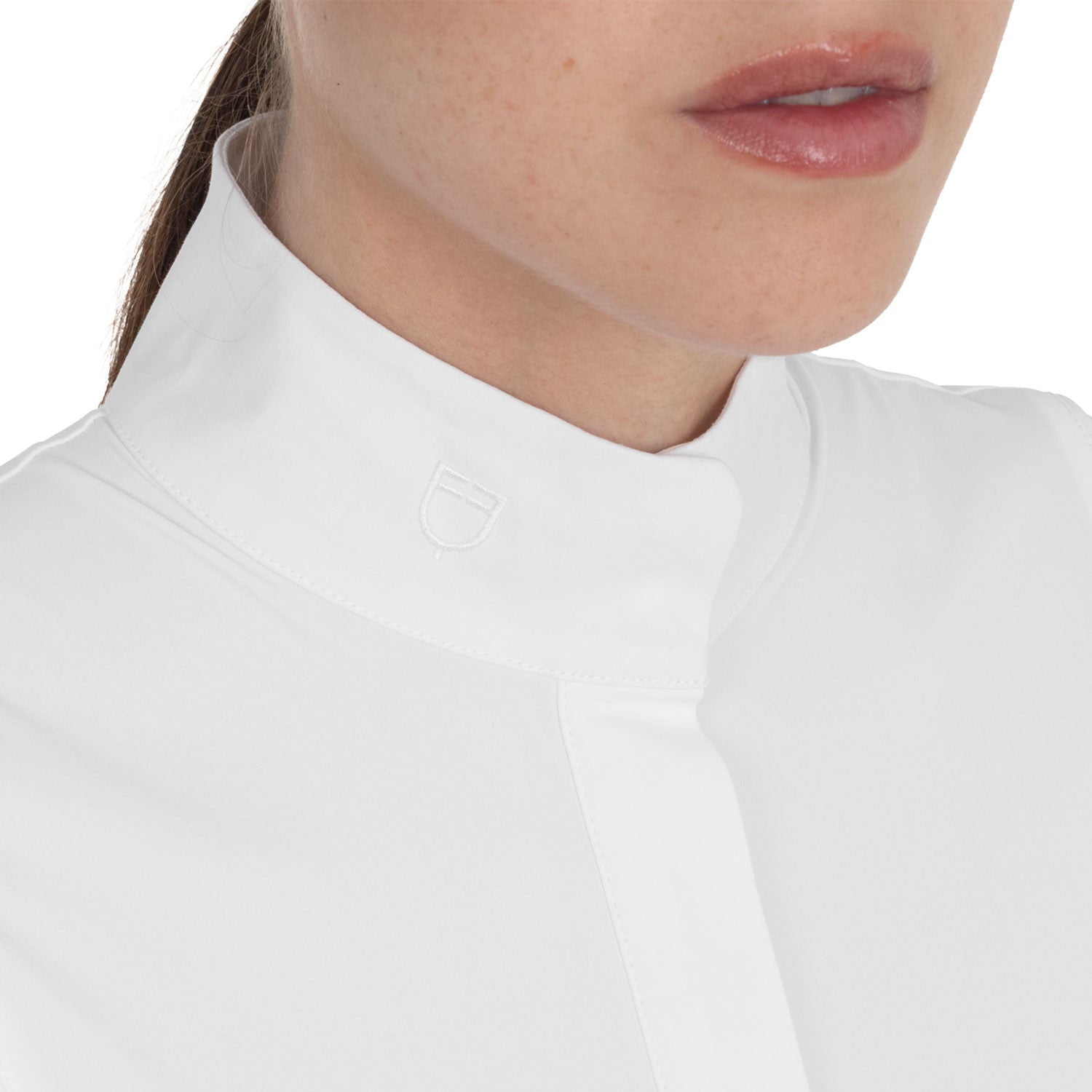 Close-up view of the Equestro logo on the collar of the White Equestro Perforated Long-Sleeve Competition Polo Shirt as worn by a female model
