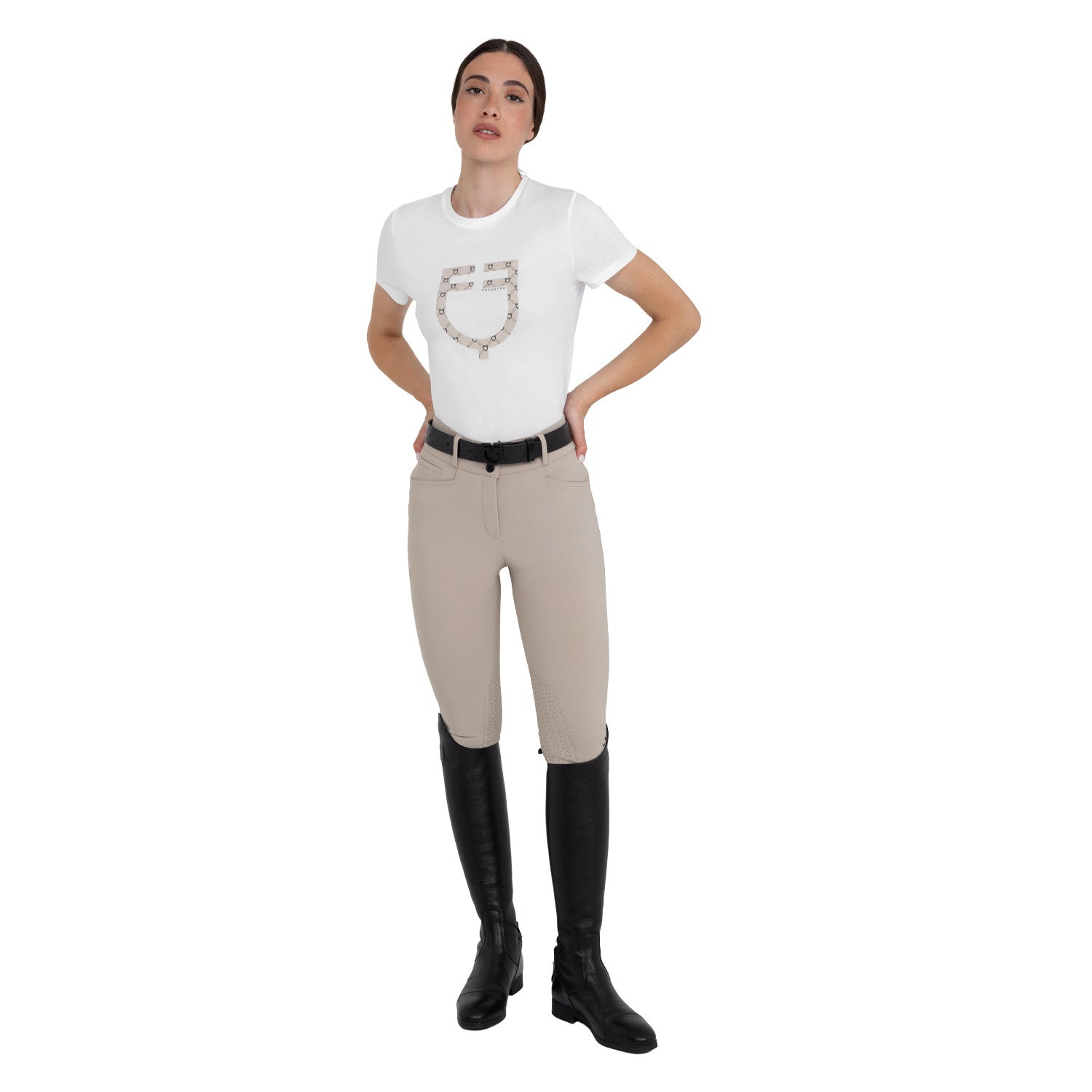 Full body front view of a female model wearing the Cobblestone Equestro High-Waisted Knee Grip Breeches with a white tshirt on a plain background