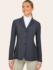 A woman wearing a dark gray tailored blazer over a white shirt and beige pants stands facing slightly to the side and smiles.