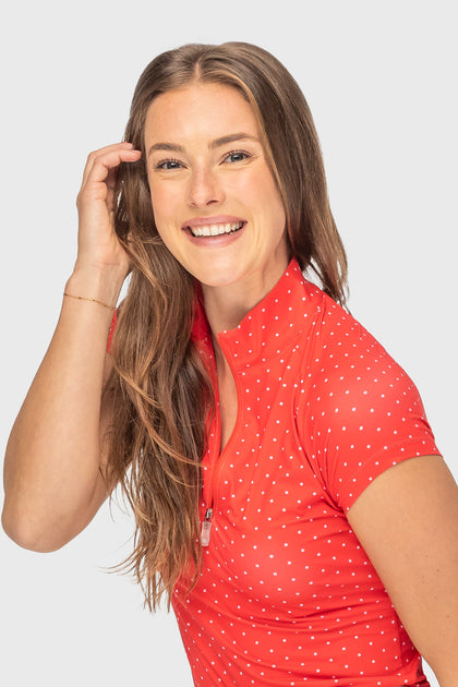 Angled front view of a female model wearing the red & pink swiss dot Kastel Cap Sleeve 1/4 Zip Sun Shirt on a plain background