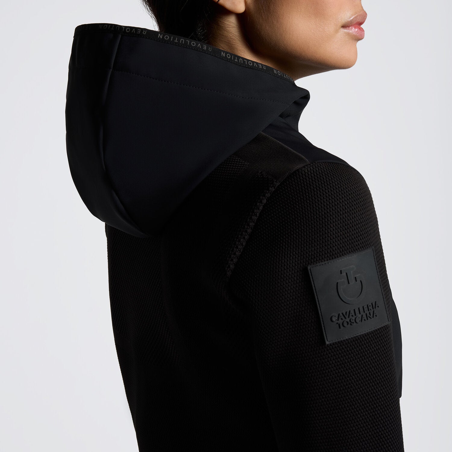 Black full zip softshell jacket with hood and shoulder logo shown on model in front of plain white background