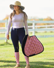 Front view of a female model wearing the Dreamers & Schemers Hay Sunshine F Bomb Hat while holding a pink saddle pad and standing in the grass