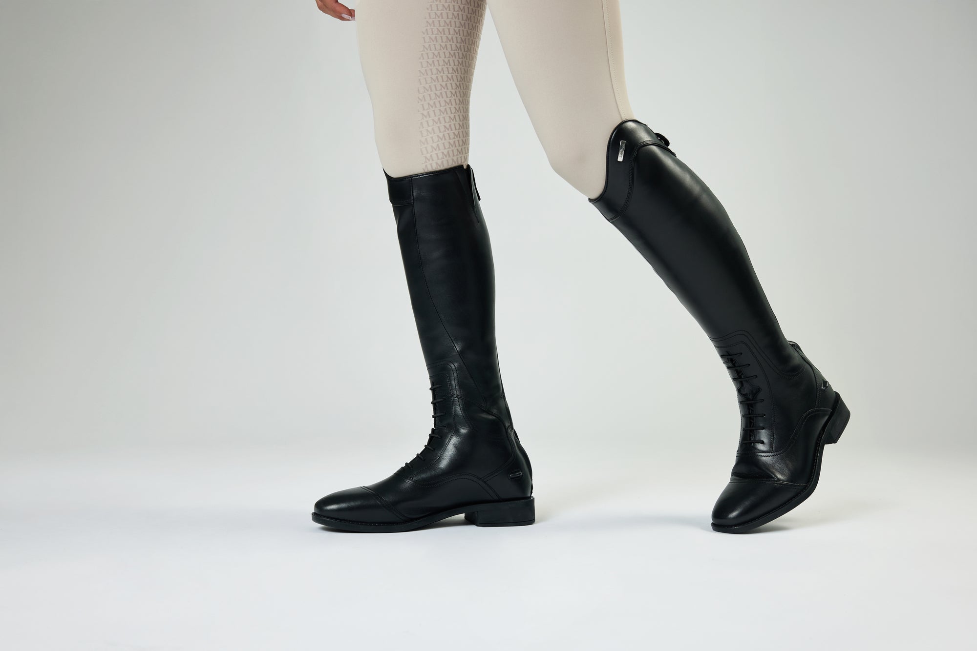 Side view of a model wearing a black pair of LeMieux Junior Field Riding Boots on a plain background