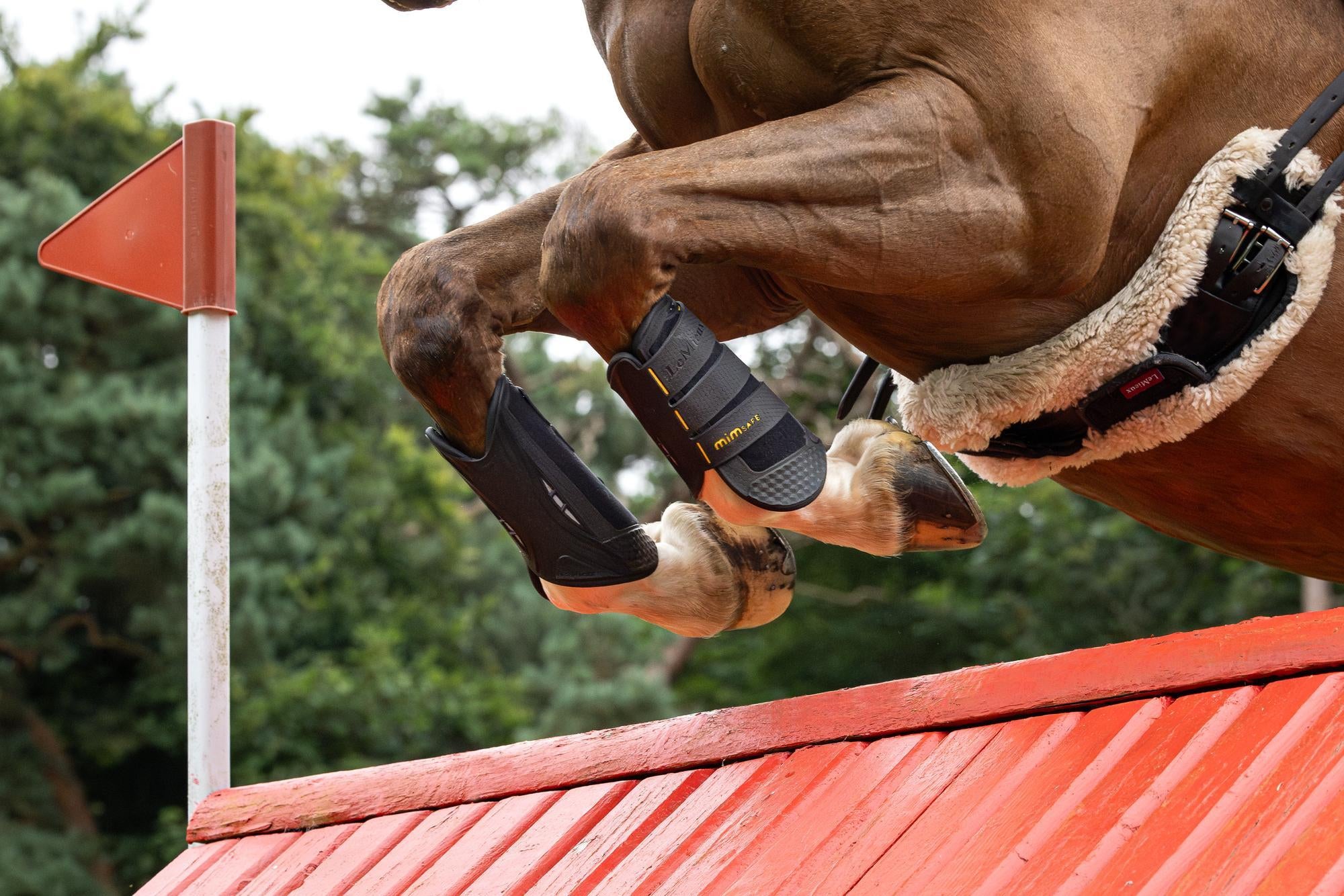 Side view of a horse wearing the LeMieux MIMsafe XC Front Boots while jumping over a jump outside