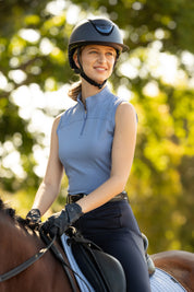 LeMieux Airflow sleeveless base layer in powder blue with quarter-zip high collar, worn while riding a horse with a black helmet and gloves outdoors.