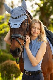 LeMieux Airflow sleeveless base layer in powder blue with quarter-zip high collar, worn while standing beside a bridled horse outdoors.
