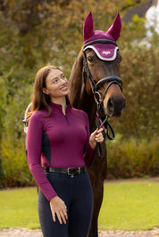 Front view of a model standing outside in front of a horse that is wearing the Blackberry LeMieux Loire Fly Hood