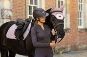 View of a female model wearing the Cocoa LeMieux Heritage Check Long Sleeve Base Layer while standing in front of a black horse
