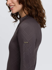 Side view of a female model wearing the Cocoa LeMieux Heritage Check Long Sleeve Base Layer on a plain background