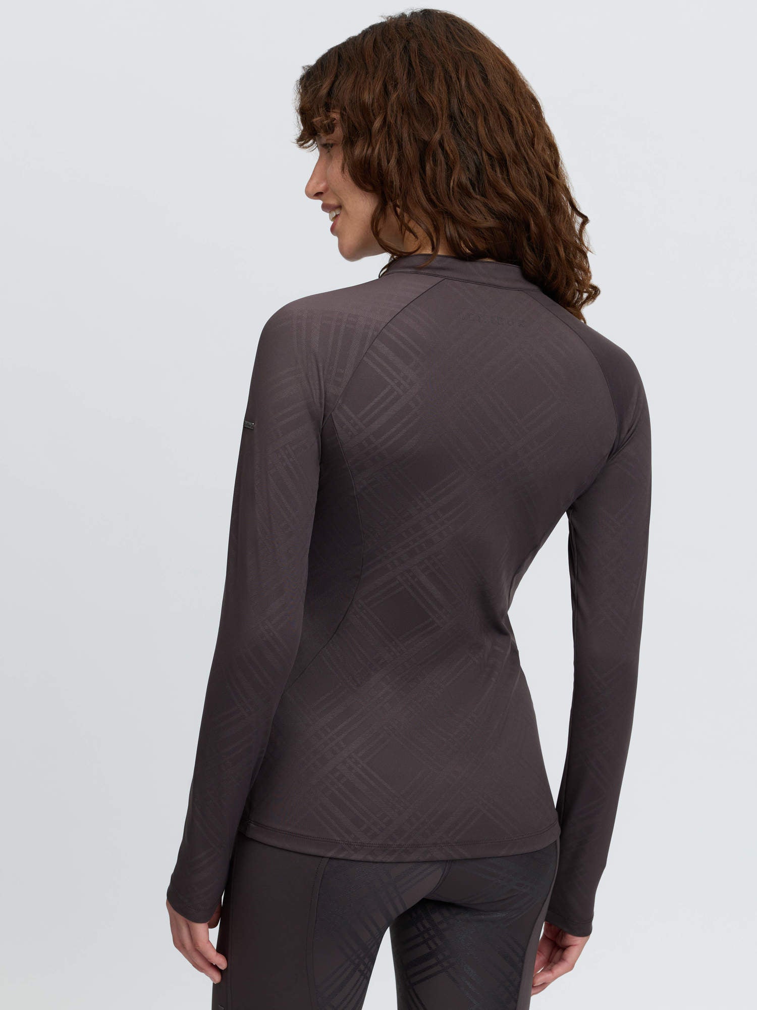 Back view of a female model wearing the Cocoa LeMieux Heritage Check Long Sleeve Base Layer on a plain background