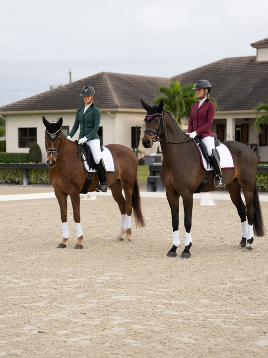 Front view of 2 models sitting on horses in an outdoor arena - one model is wearing the Sycamore Green Equestrian Stockholm Classic Show Jacket and the other is wearing the Merlot Equestrian Stockholm Classic Show Jacket