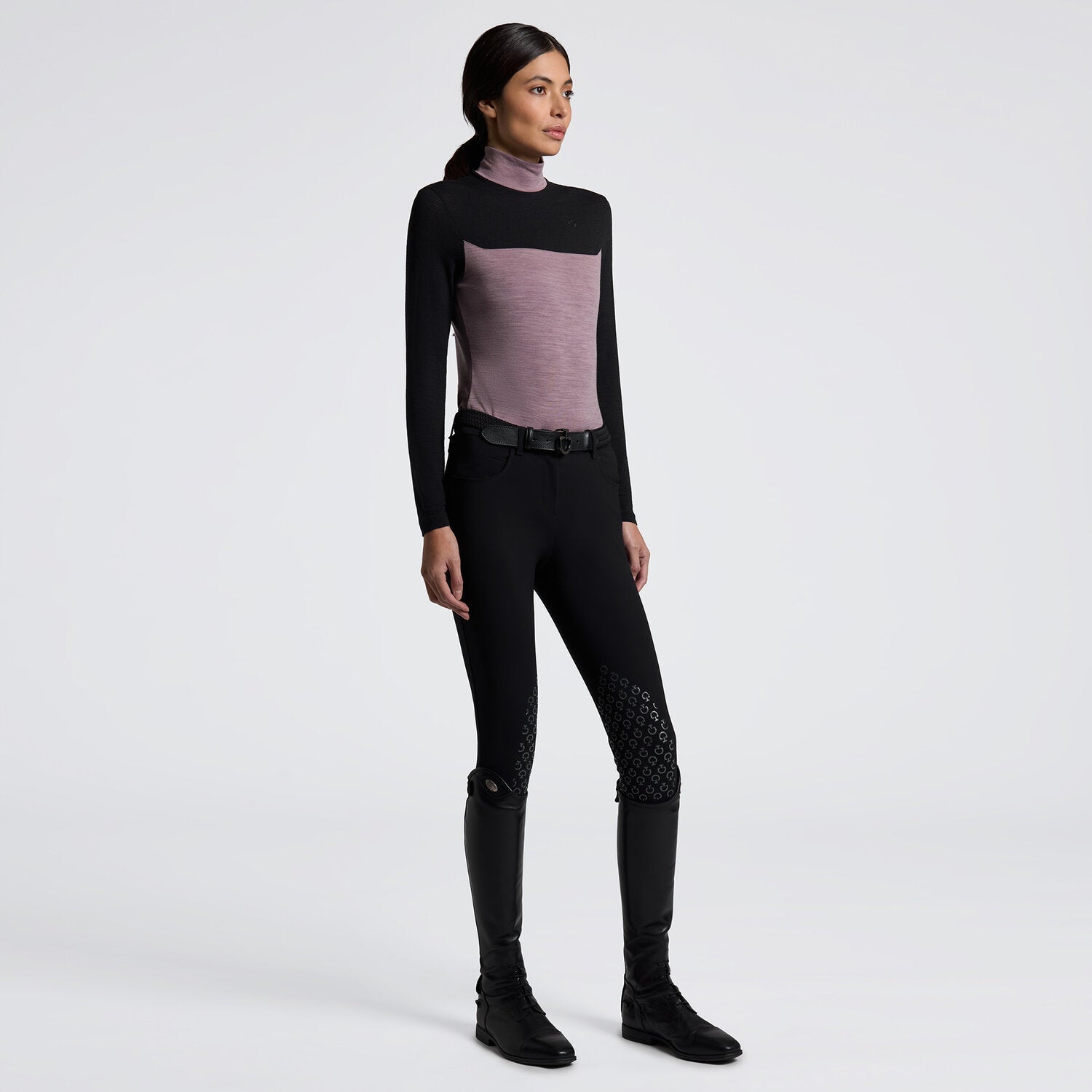 Angled full body front view of a female model wearing the Grape Shake Cavalleria Toscana Long Sleeve Tech Wool Turtleneck Training Polo with black breeches on a plain background