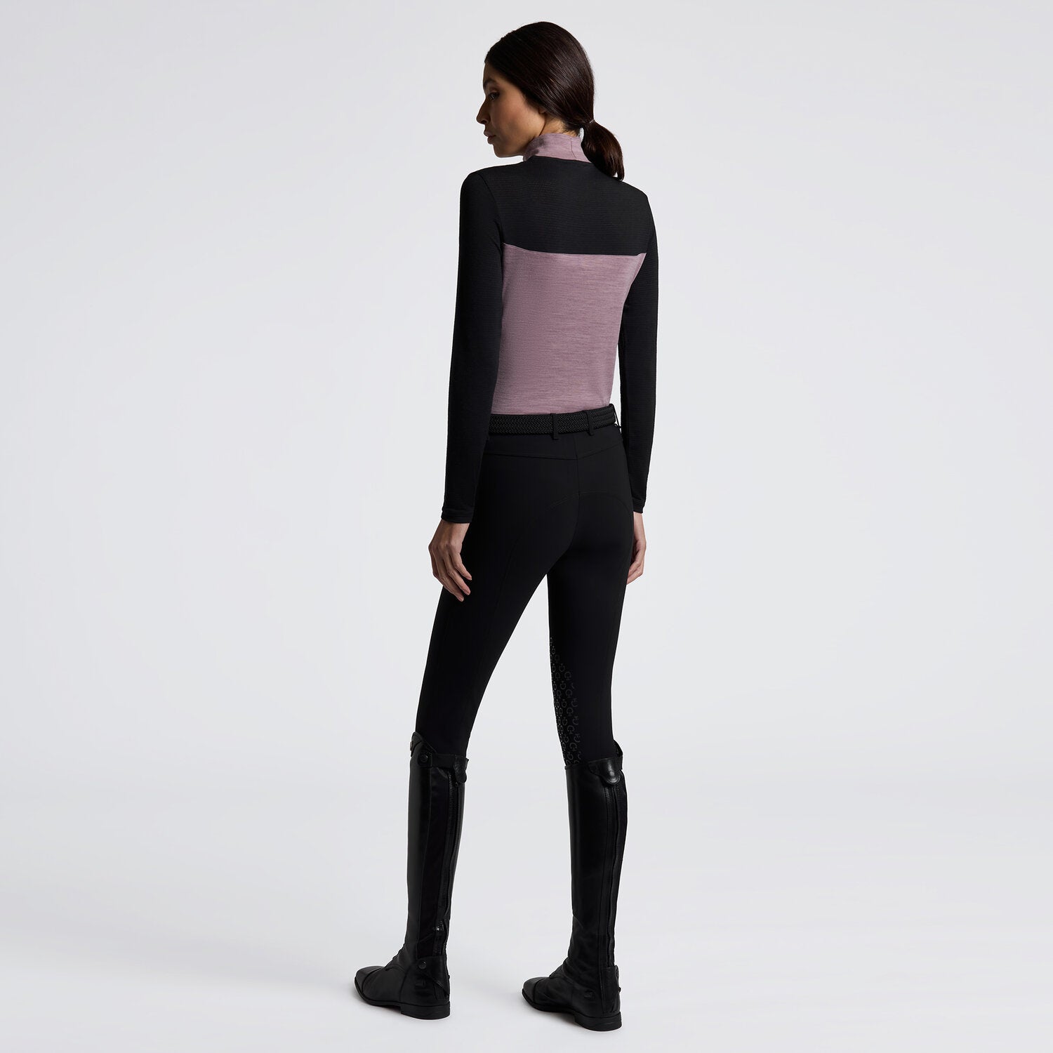 Angled full body back view of a female model wearing the Grape Shake Cavalleria Toscana Long Sleeve Tech Wool Turtleneck Training Polo with black breeches on a plain background