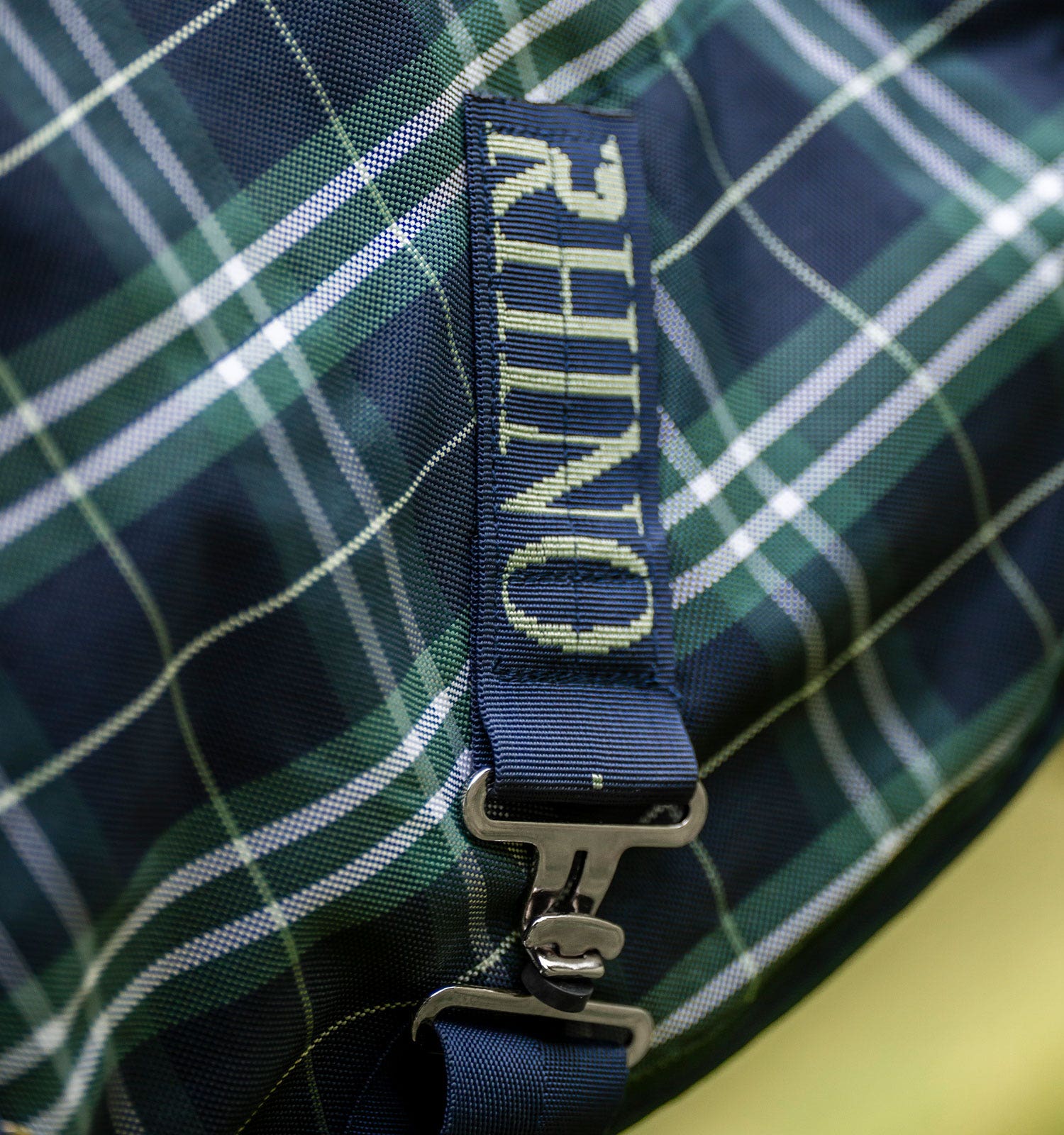 Close-up view of the RHINO logo on the surcingle attachment on the Hunter Check/Green & Navy Horseware Rhino Plus Turnout 0g