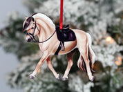 Front view of the Dun Fjord Classy Equine Under Saddle Horse Ornament hanging in front of a tree